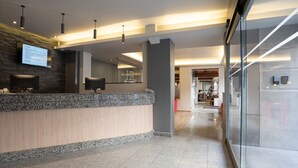 Un moderno área de recepción de hotel con mostrador de granito, pantalla digital y pared de vidrio.