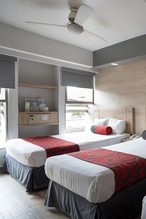 A hotel room with two beds, a ceiling fan, a window with curtains, a bedside table, and a small cabinet. - Hotel Roble (Mexico City)