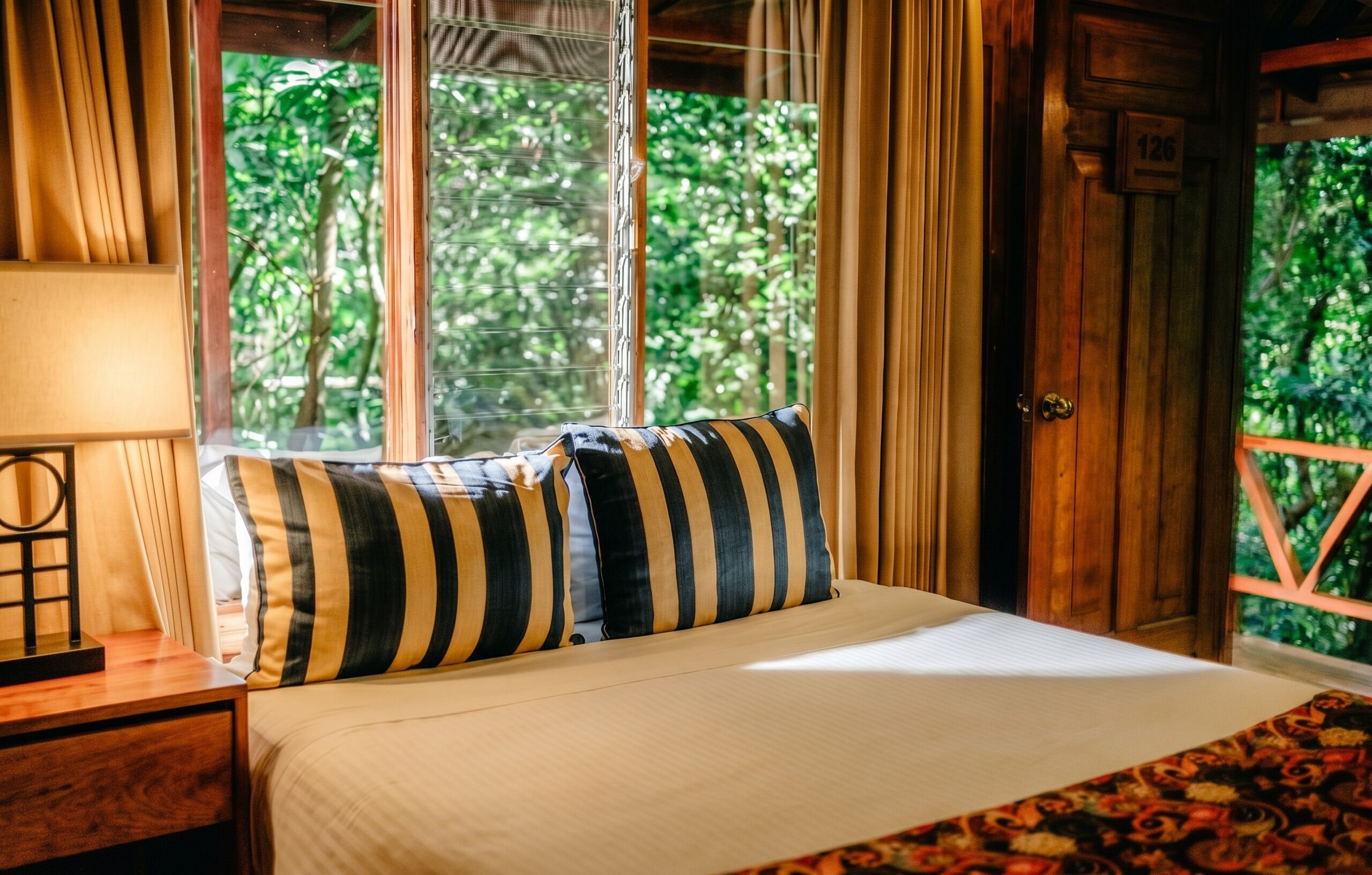 Una cama con almohadas a rayas, una mesita de noche de madera, una lámpara y una ventana con cortinas.