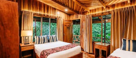Una habitación con paneles de madera, dos camas, una mesita de noche con lámpara y una ventana con cortinas.