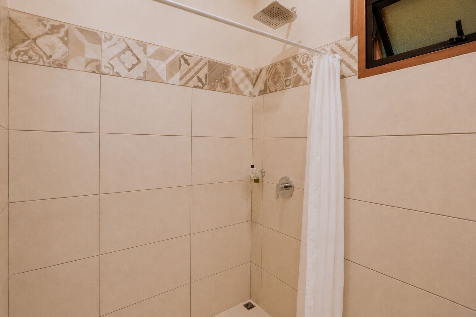 A shower area with a showerhead, a curtain, and a tiled wall.