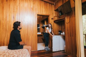 A wooden-paneled room with a bed, a small kitchenette, and a TV mounted on the wall. - Jaguarundi Lodge (Monteverde)