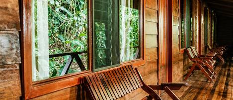 A row of wooden benches along a corridor with large windows overlooking greenery.