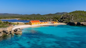 Een kusthotel met een rij oranje gebouwen, een zandstrand en helder turquoise water.