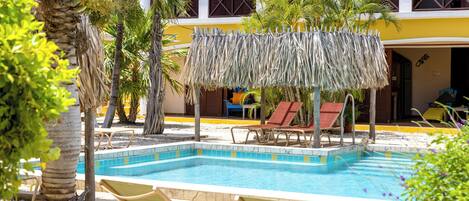 A pool area with lounge chairs, a thatched roof structure, and palm trees.