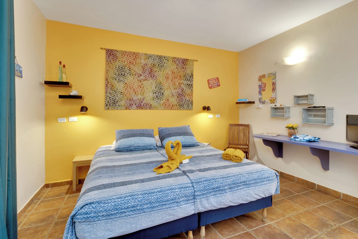 Ein Schlafzimmer mit einem Bett, einem Nachttisch, einer Wandablage mit Toilettenartikeln, einem dekorativen Wandteppich und einem kleinen Tisch mit einer Vase.