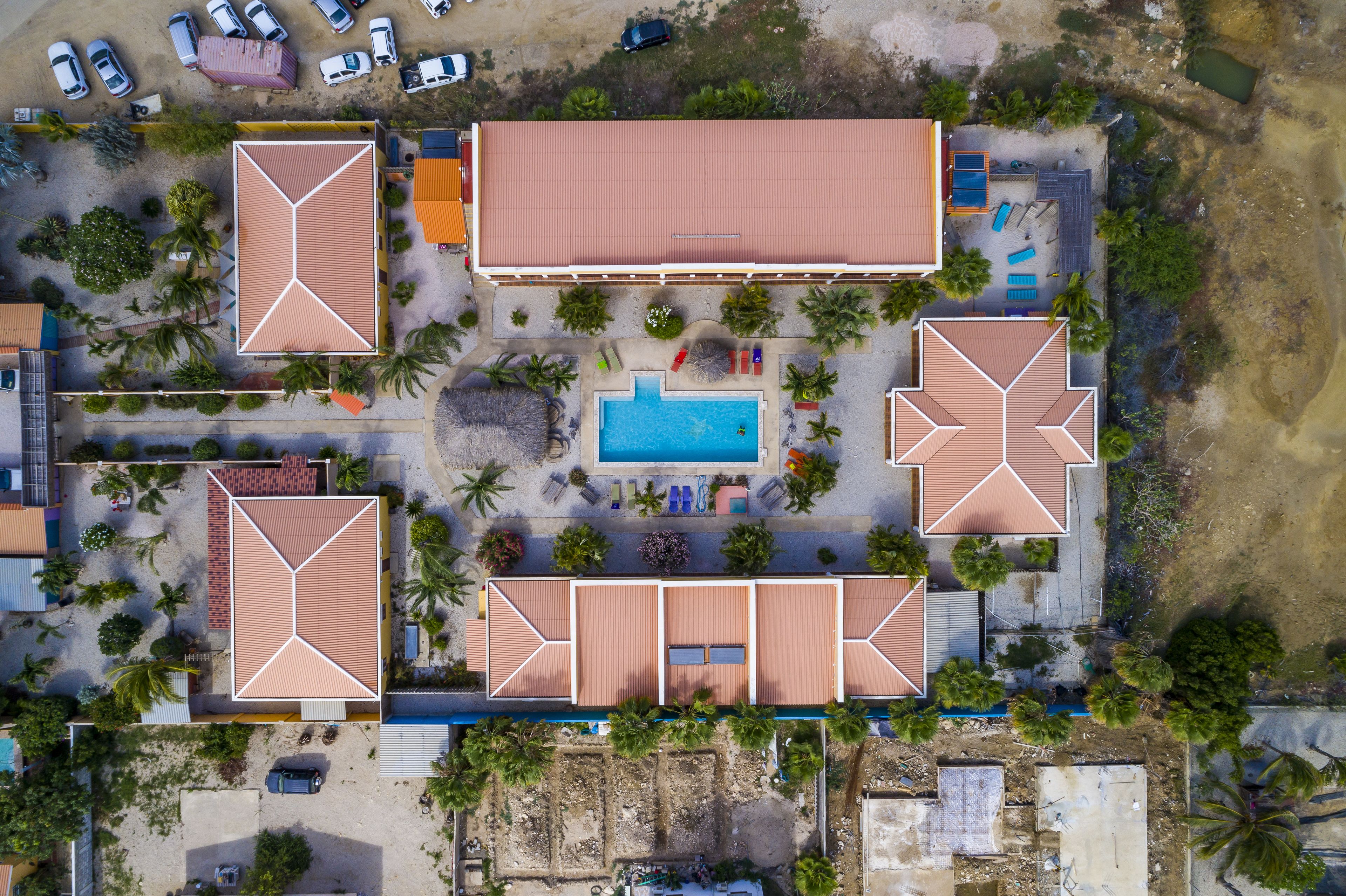 An aerial view of a resort with multiple buildings, a swimming pool, and palm trees.