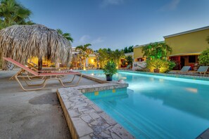 A pool area with lounge chairs and a thatched structure. - Djambo Apartments - Adults Only (Kralendijk)