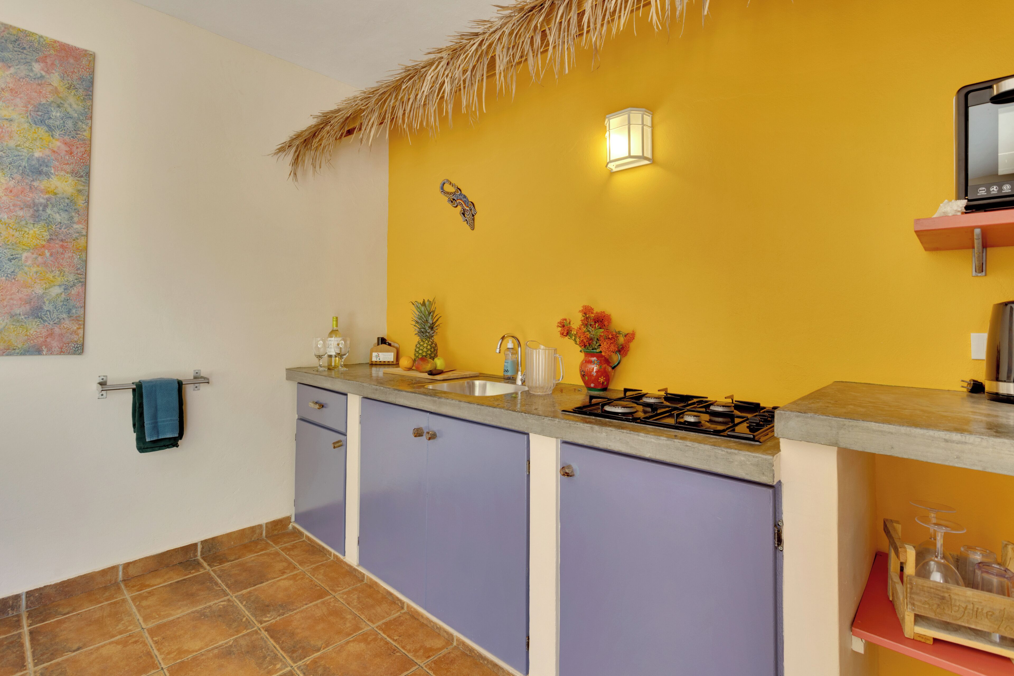 Une cuisine avec un mur jaune, un toit de chaume, un évier, une cuisinière et des placards.