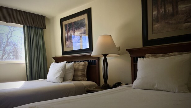 Quarto de hotel com duas camas, uma mesa de cabeceira, uma luminária e um quadro na parede.
