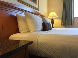 A neatly made bed with white and patterned pillows, a wooden headboard, a bedside lamp, and a checkered bedspread.