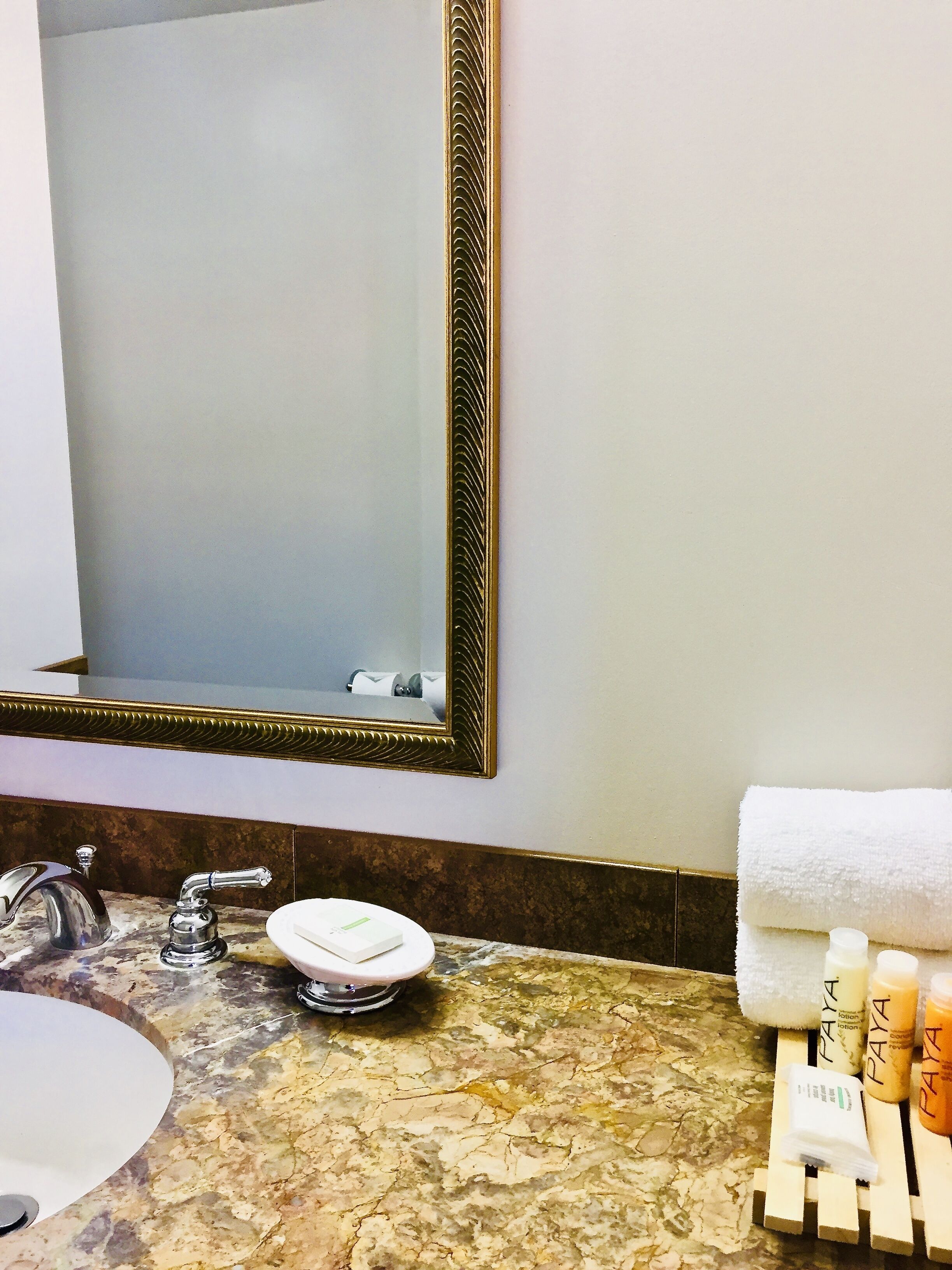 A bathroom with a marble sink, a large mirror with a decorative frame, a towel, and toiletries.