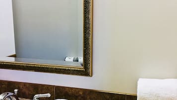 A bathroom with a marble sink, a large mirror with a decorative frame, a towel, and toiletries.