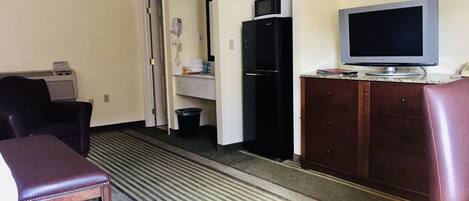 A hotel room with a bed, a desk, a chair, a television, a refrigerator, and a microwave.