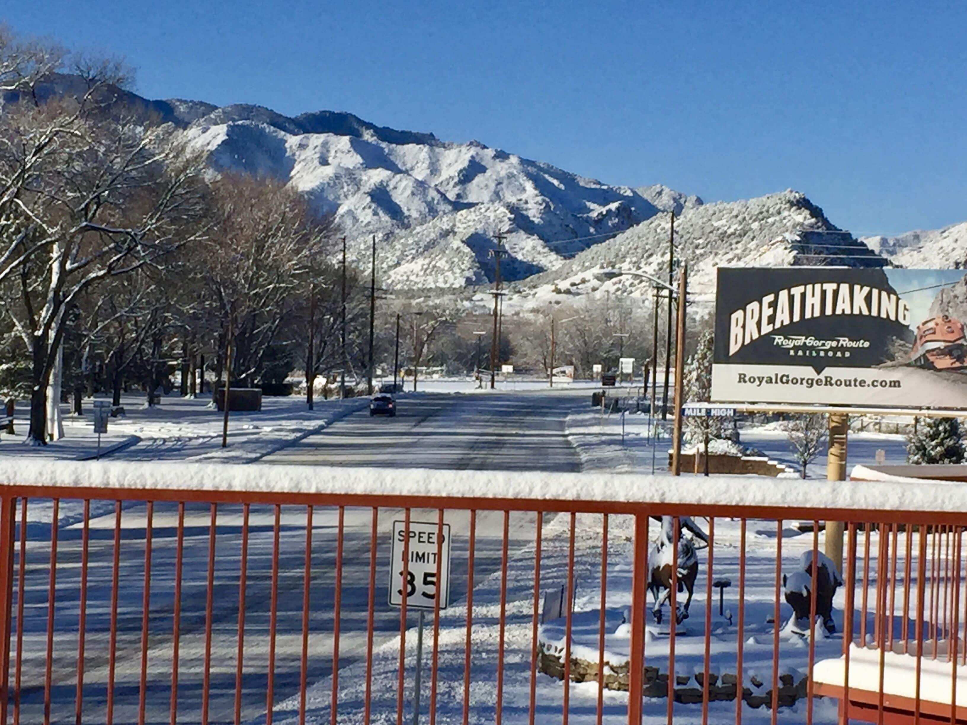 A snow-covered street with a speed limit sign of 35 mph, a sign for the Royal Gorge Route Railroad, and a mountain in the background.