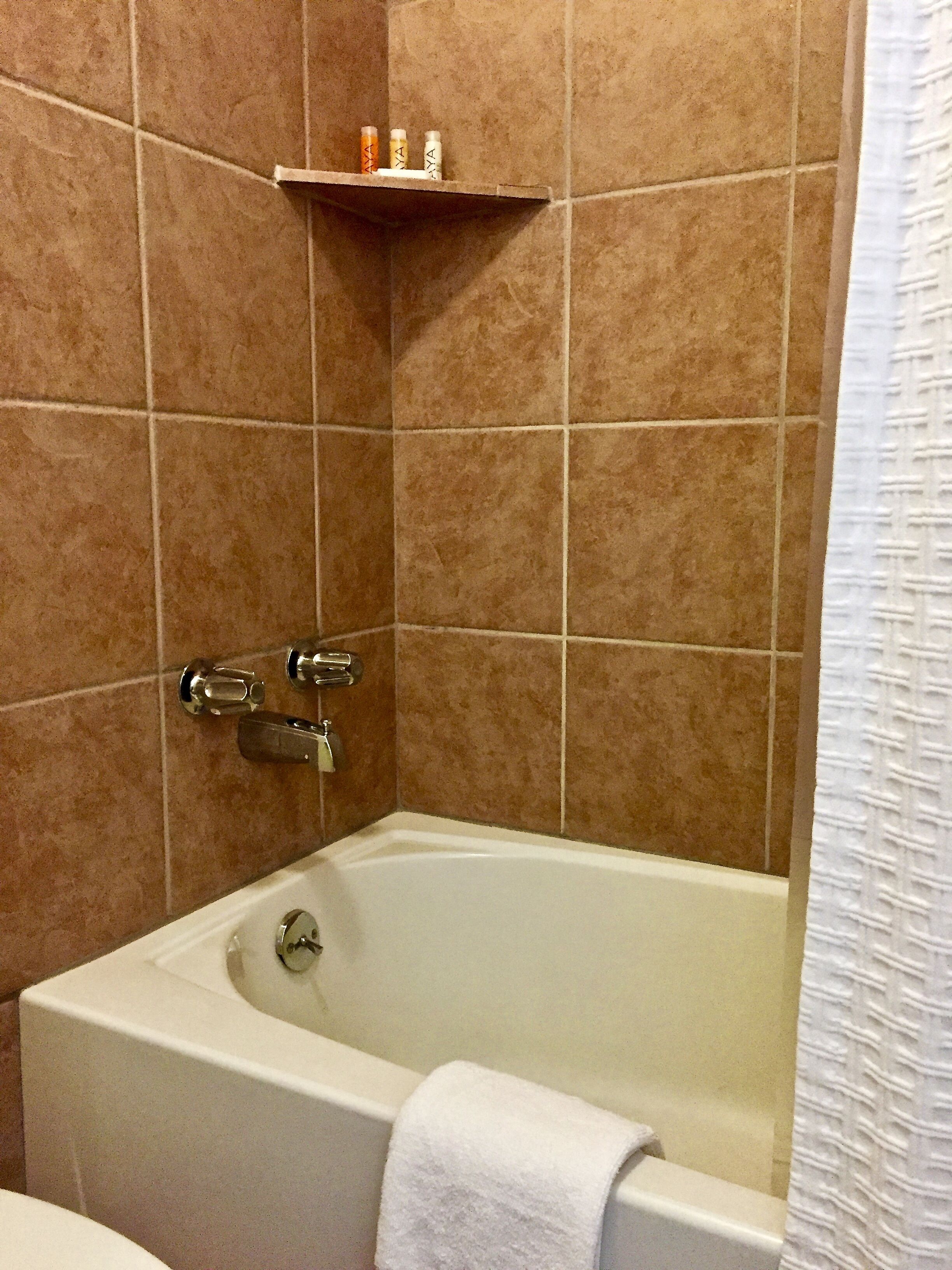 A bathroom with a bathtub, a shower, and a shelf with toiletries.