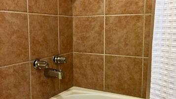 A bathroom with a bathtub, a shower, and a shelf with toiletries.