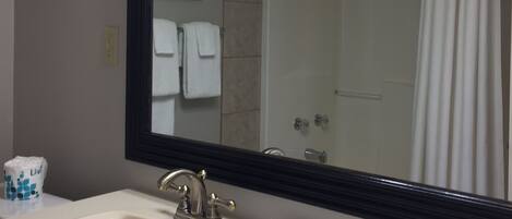 A bathroom with a large mirror, a sink, a shower, and a framed picture on the wall.