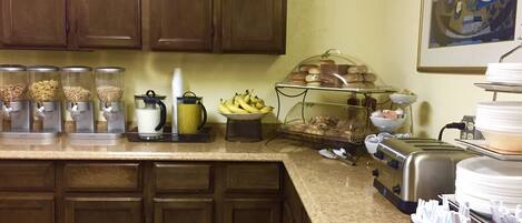 A kitchen with a buffet setup including food dispensers, a fruit bowl, and a coffee station.