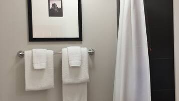A bathroom with a toilet, two towels on a rack, a framed picture on the wall, and a shower curtain.