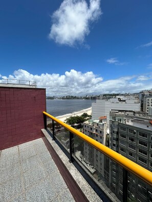 Een hoog gebouw met een gele reling, met uitzicht op een strand en stadsbeeld.