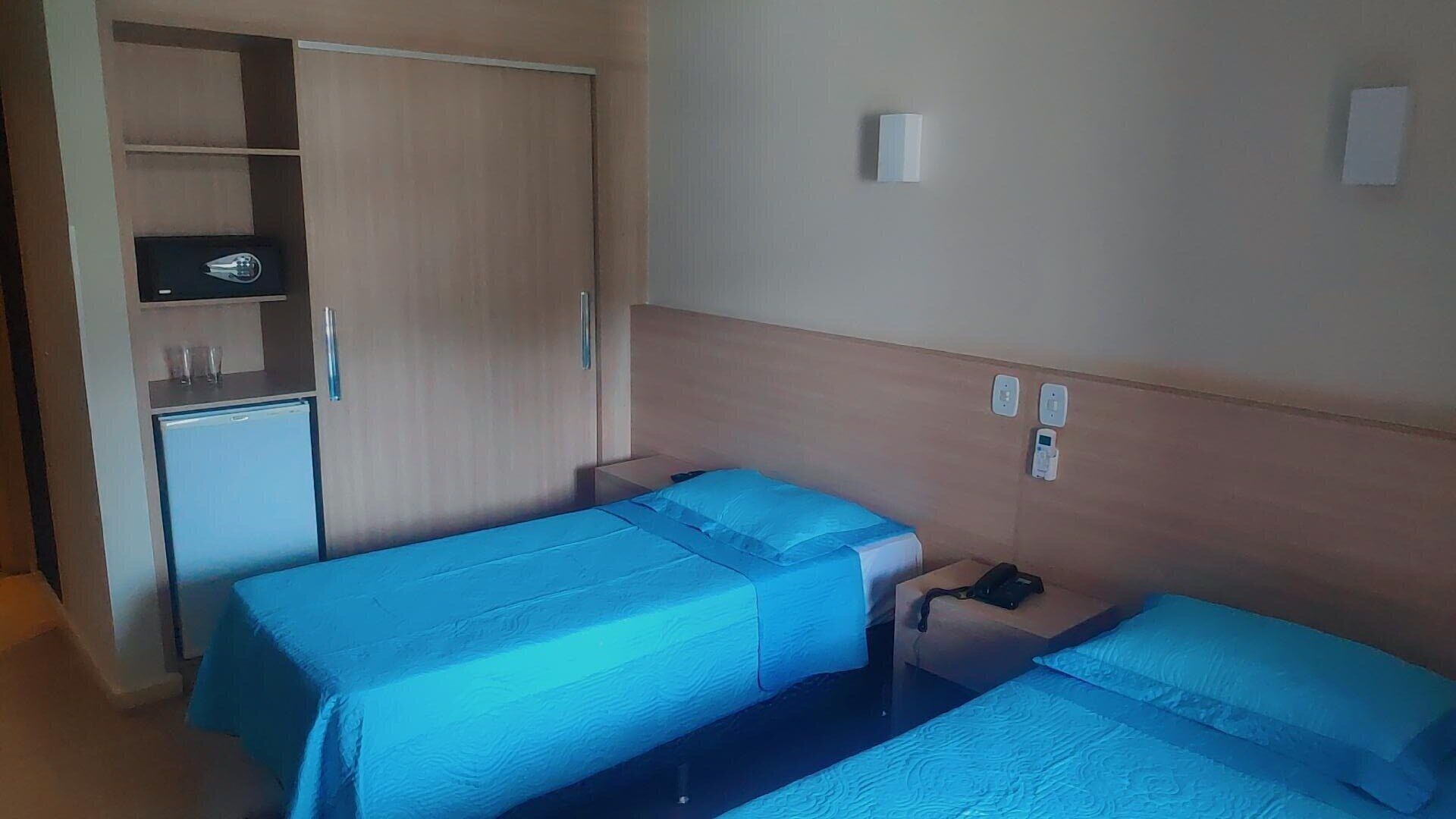 A hotel room with two single beds, a wardrobe, a small desk, and a nightstand.