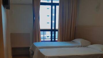 Hotellihuone, jossa on kaksi erillistä sänkyä, seinälle asennettu televisio ja ikkuna, jossa on verhot.