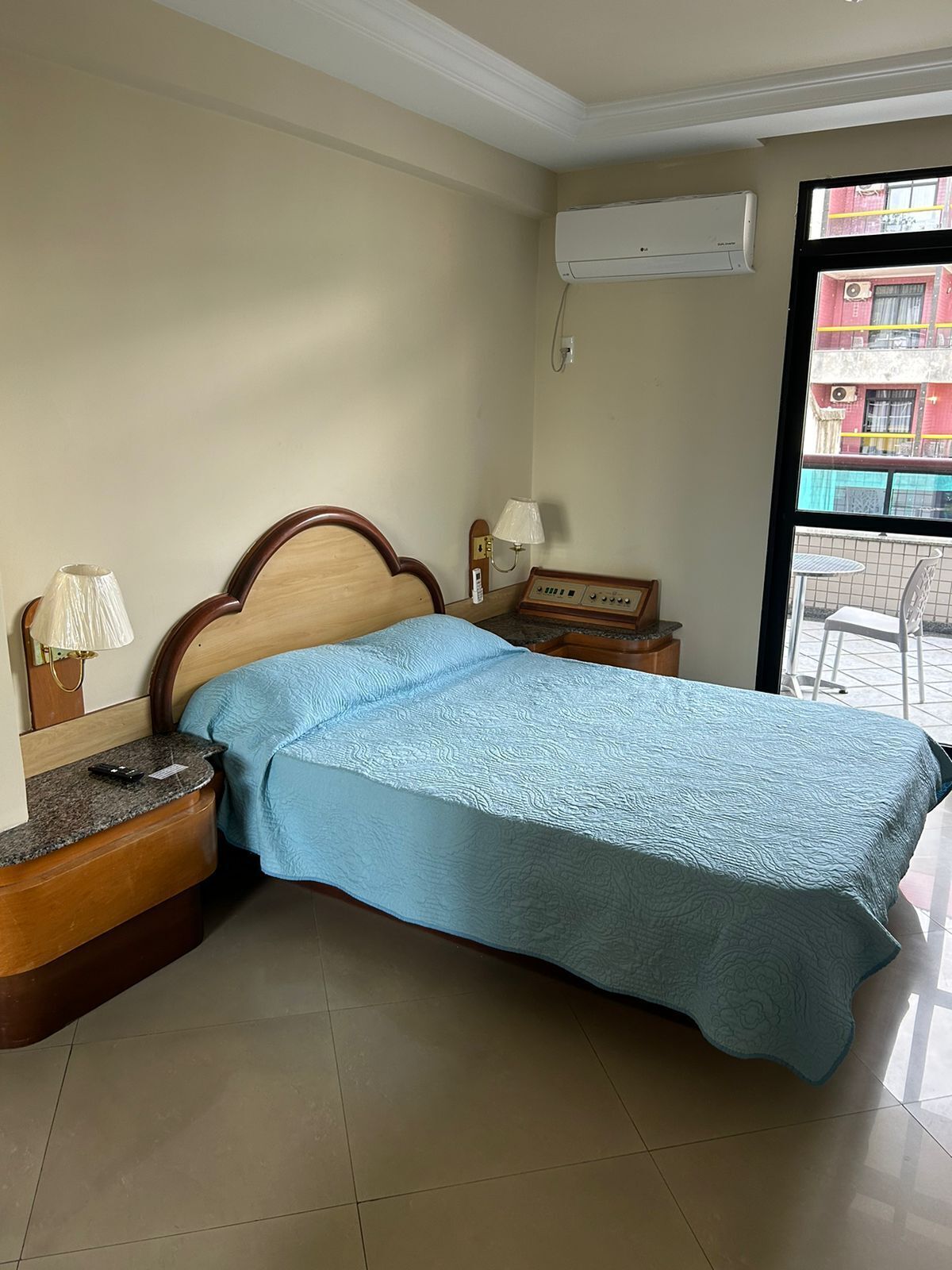 A bedroom with a bed, bedside table, lamp, and an air conditioning unit.