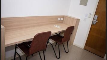 Ein kleiner, privater Raum mit einem hölzernen Schreibtisch und zwei Stühlen. Eine Tür befindet sich rechts, und ein Lichtschalter ist an der Wand angebracht.