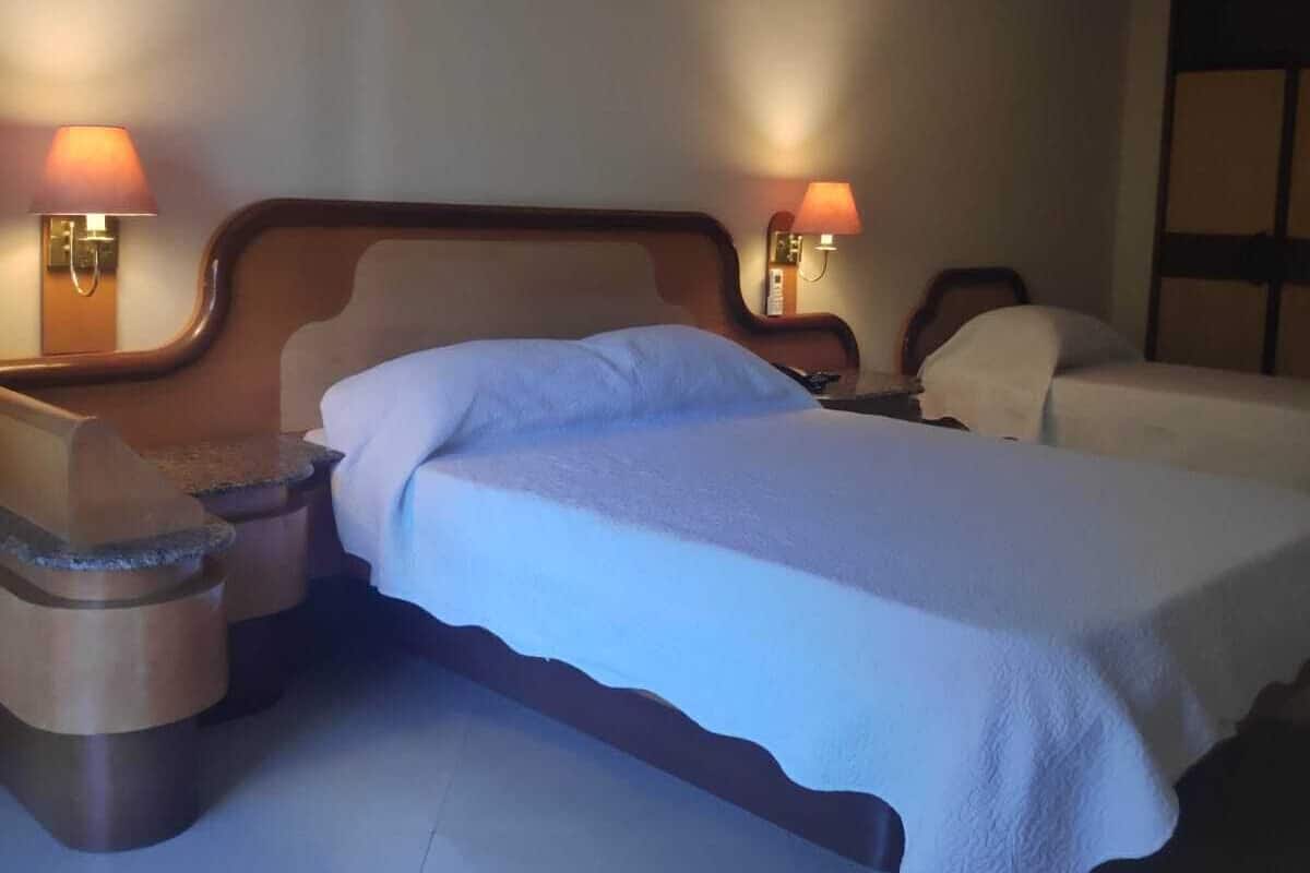 Una habitación de hotel con una cama doble, dos mesitas de noche y dos lámparas de pared.