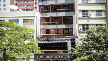 Un hotel de varios pisos con balcones, un letrero que dice 'TOWER Icarai Hotel' y un estacionamiento con automóviles.