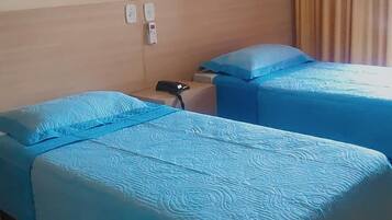 Une chambre d’hôtel avec deux lits, chacun recouvert d’une courtepointe bleue, dotée d’une tête de lit en bois, d’une table de chevet avec un téléphone et d’un rideau à la fenêtre.