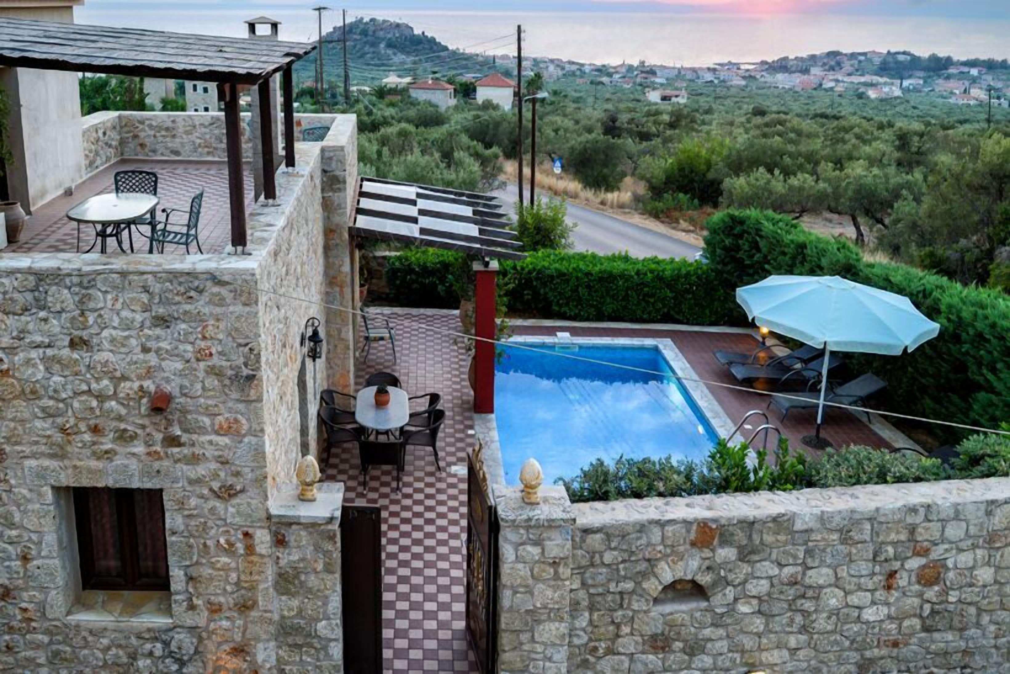 A stone terrace with a pool, outdoor seating, and a view of the countryside.