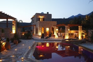 A stone building with a pool, outdoor seating, and a mountainous backdrop. - Olympia Villas (West Mani)