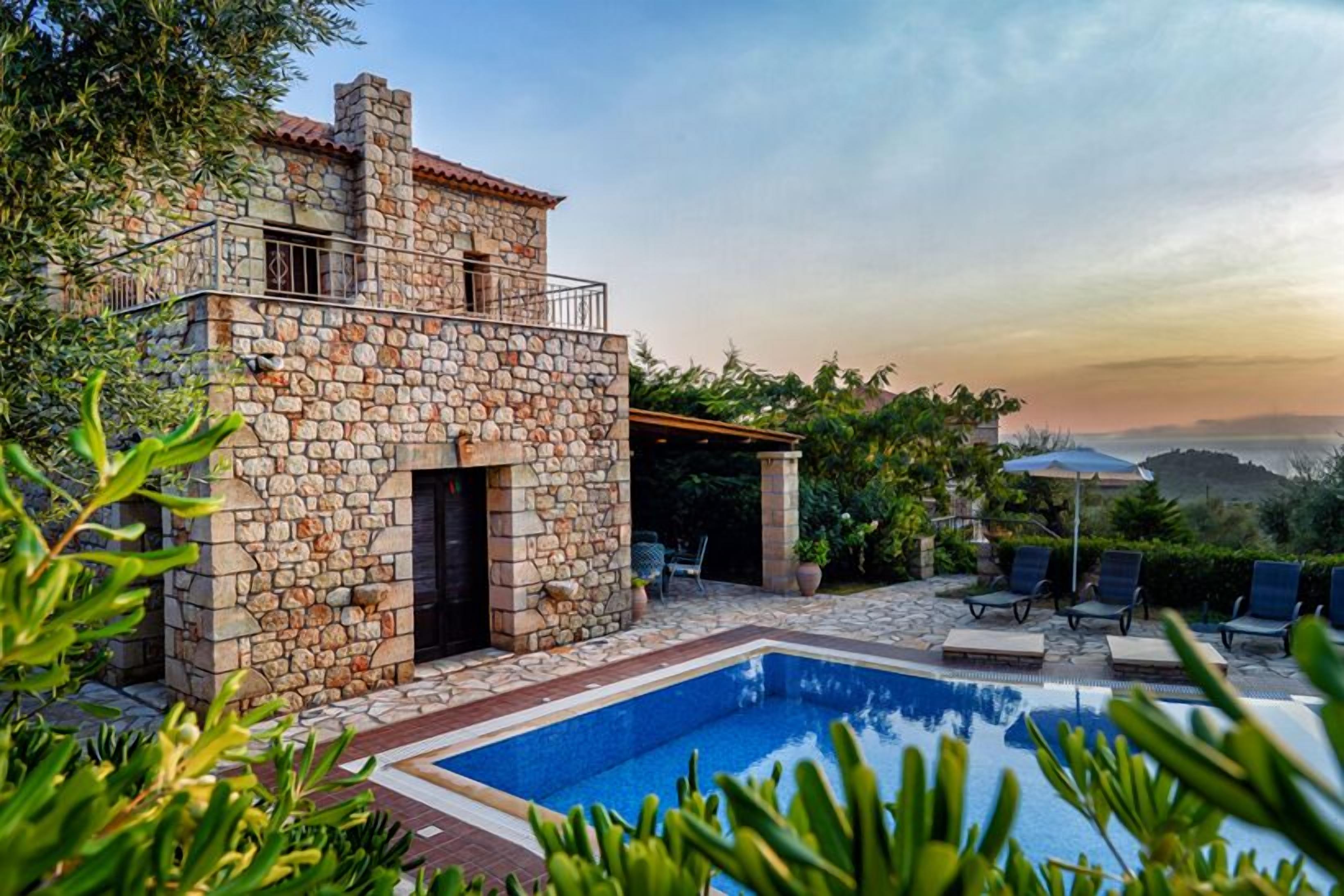 Une maison en pierre avec une piscine, un espace extérieur aménagé et une vue sur les collines.