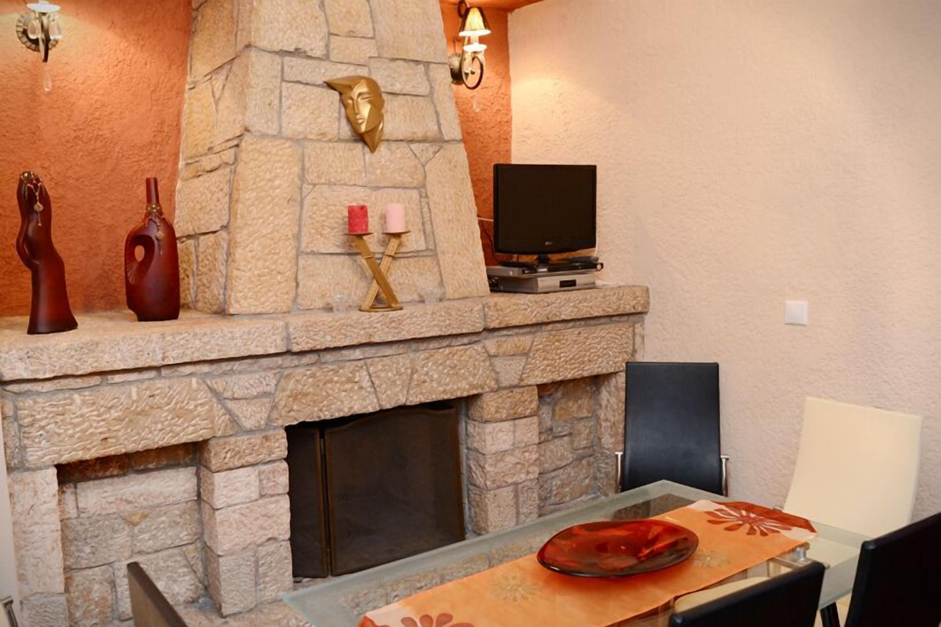 Une cheminée en pierre agrémentée d’objets décoratifs, un téléviseur à écran plat et une table en verre avec un set de table.