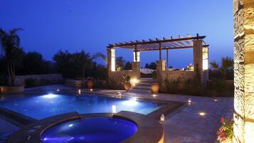 A swimming pool with a hot tub, stone walls, and a pergola with lights.