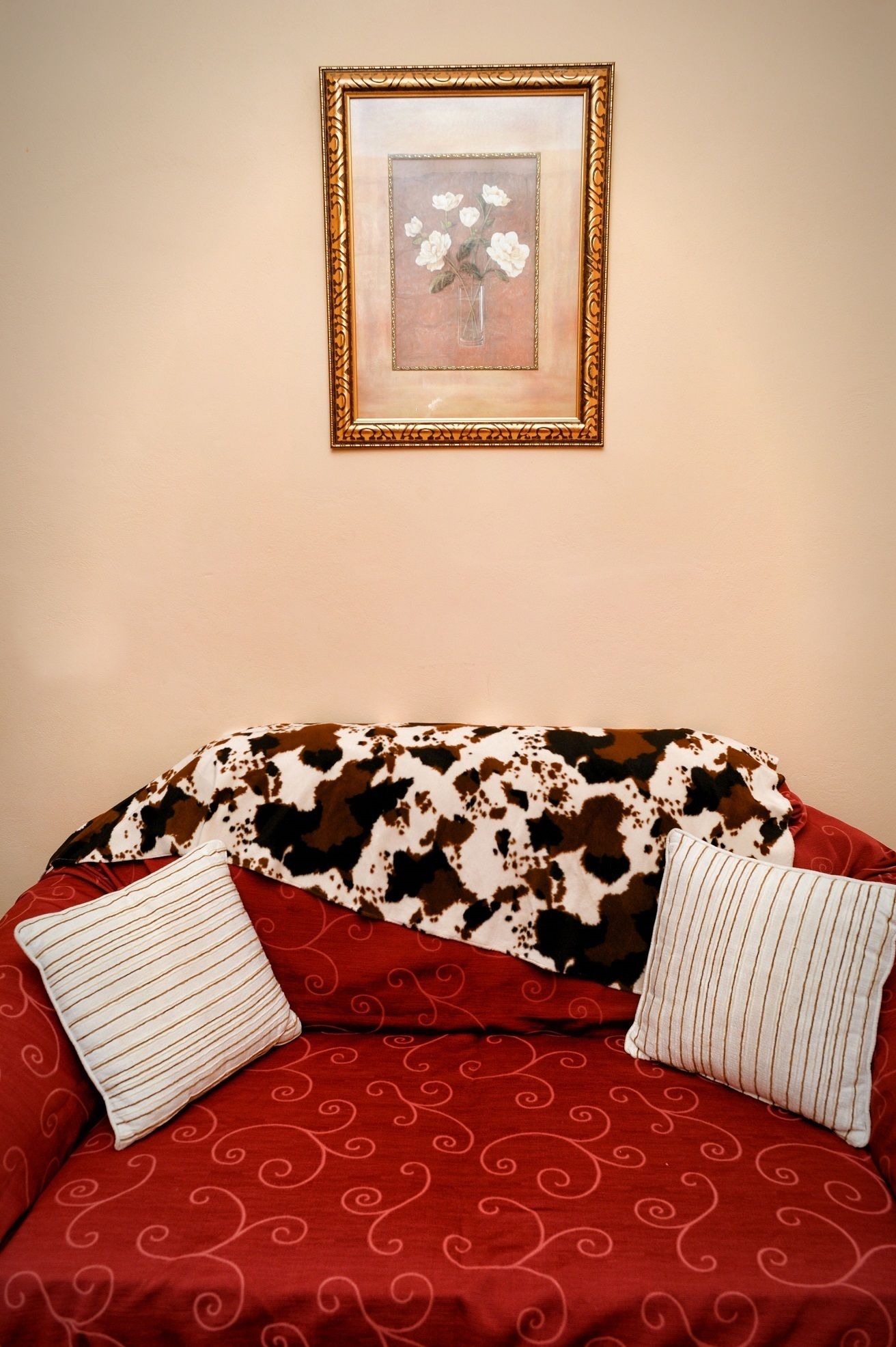 A sofa with a cow print and red fabric, two pillows, and a framed picture on the wall.