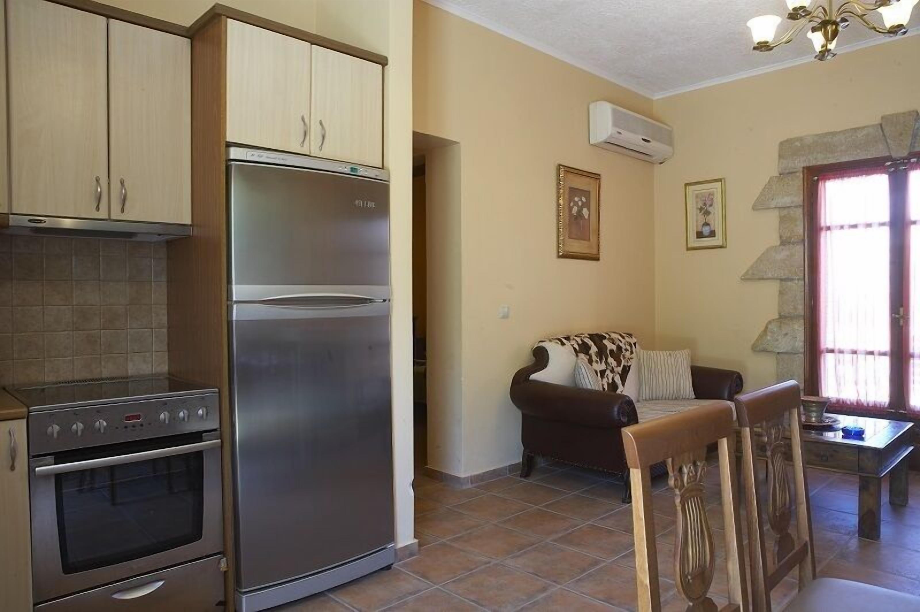 A kitchen with a refrigerator, oven, and cabinets. There is a living area with a sofa and a table.