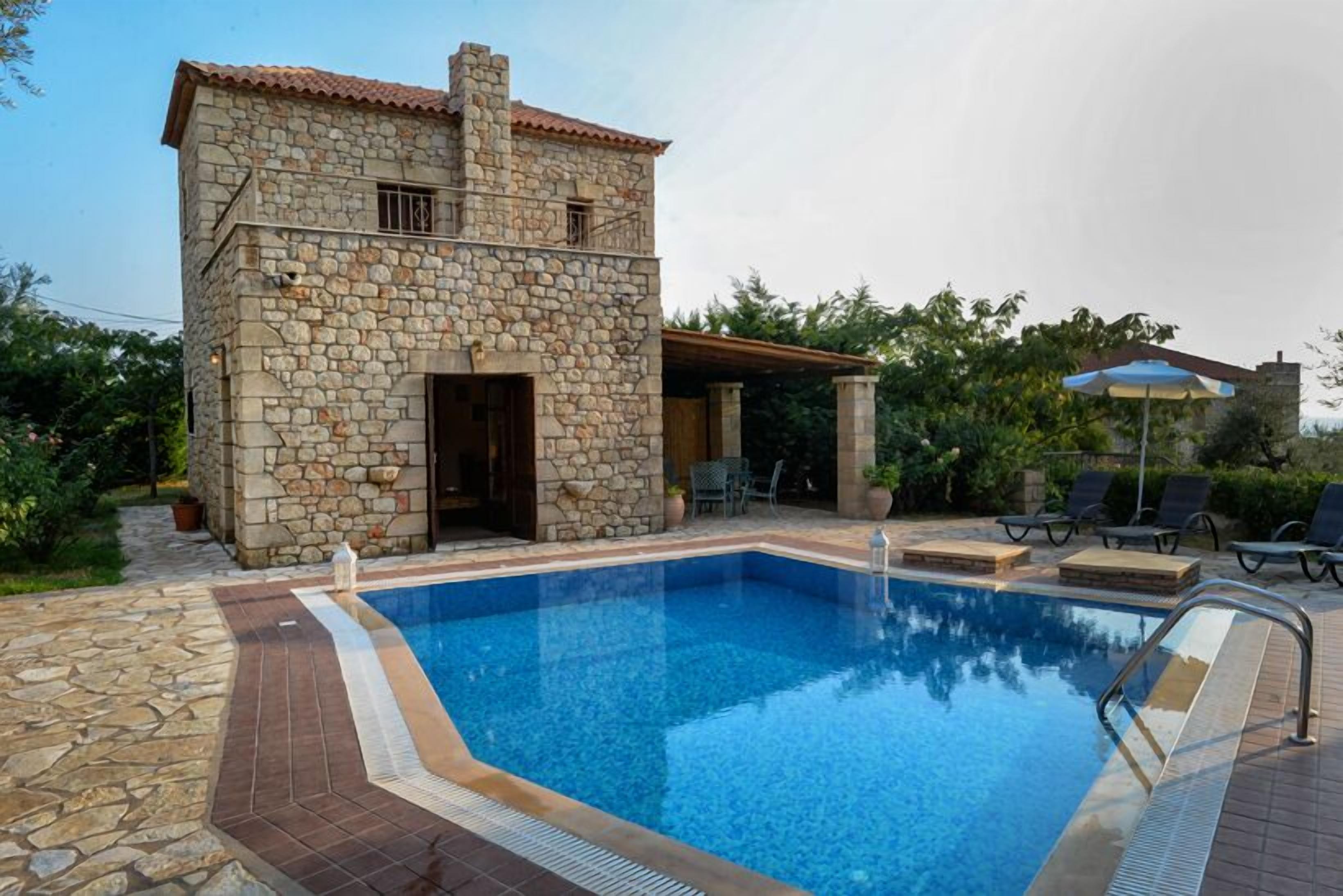 A stone building with a swimming pool, outdoor seating, and a covered patio area.