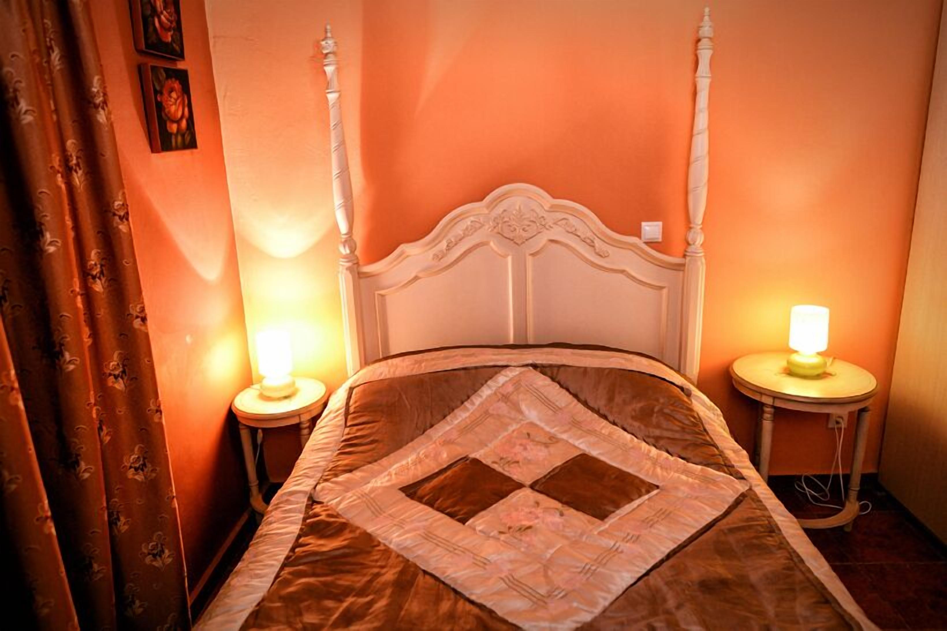 A bed with a quilt, two bedside lamps, and a curtain.