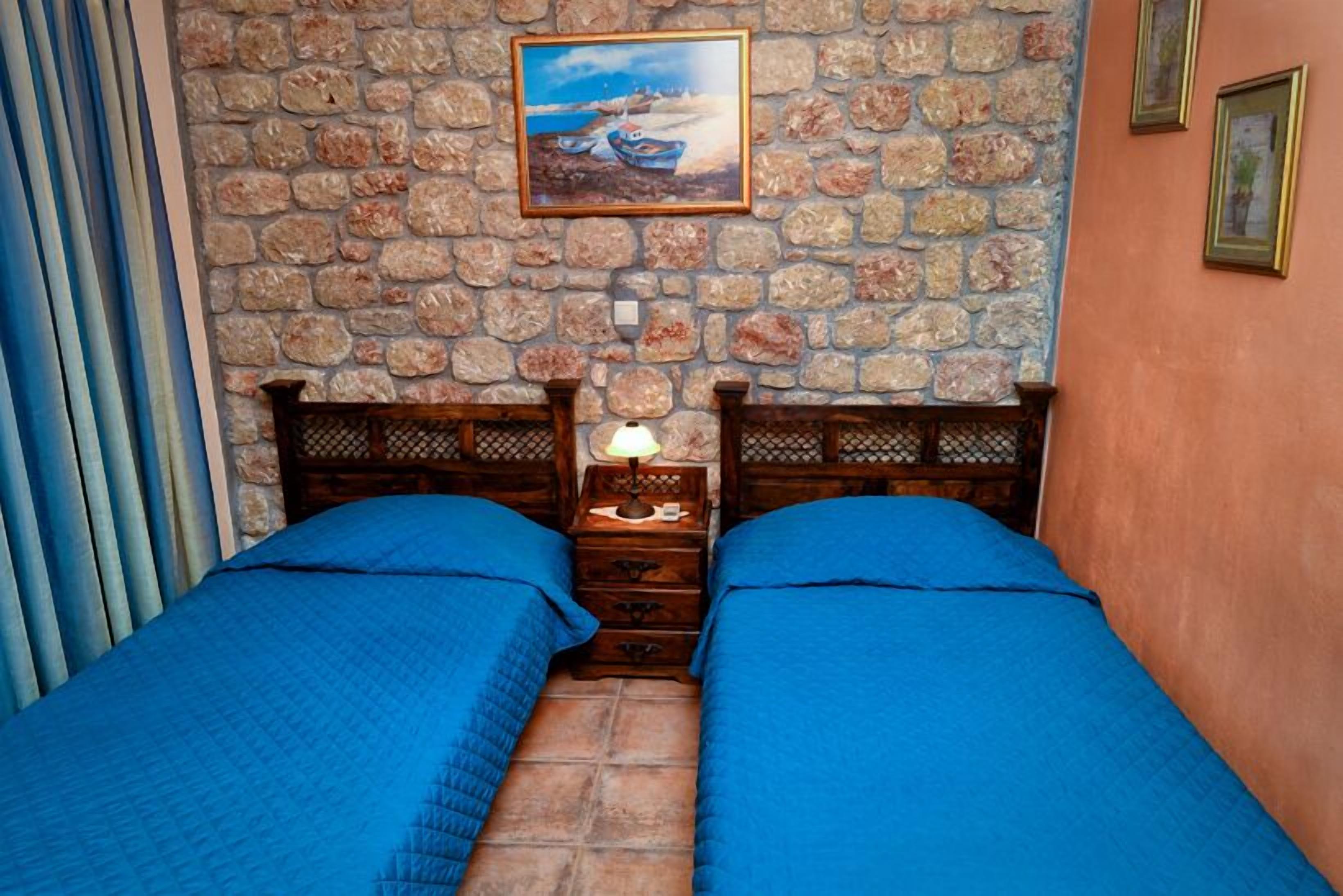 Una habitación con dos camas, una pared de piedra, un cuadro y un cabecero de madera.