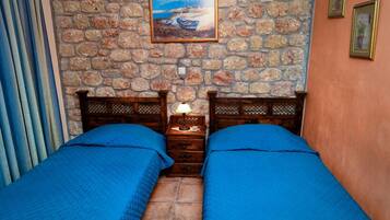 Una habitación con dos camas, una pared de piedra, un cuadro y un cabecero de madera.