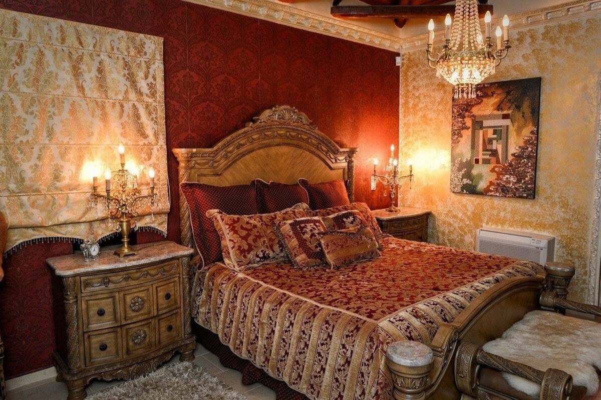 Un dormitorio clásico con una cama grande, un cabecero decorado y una araña.