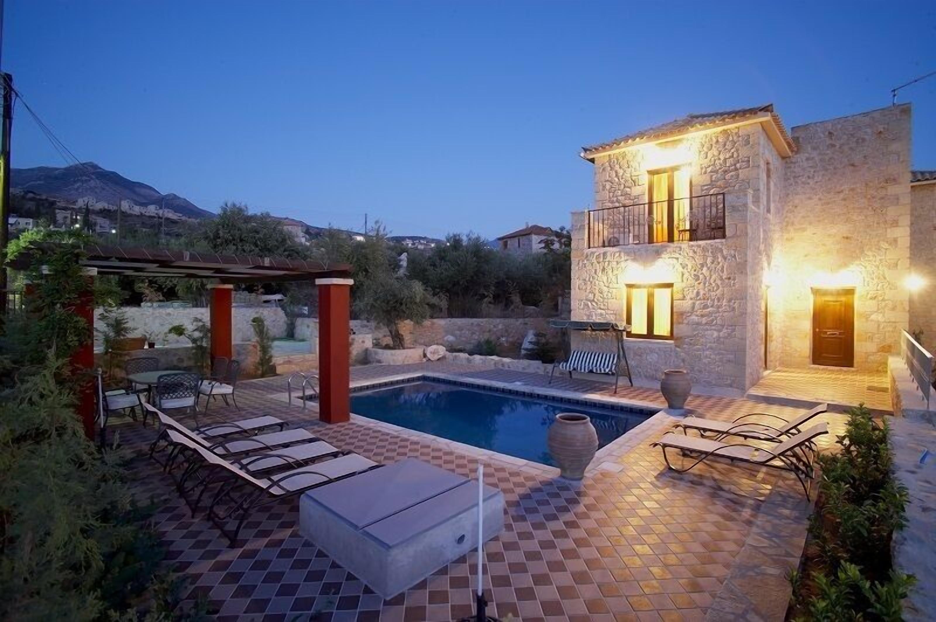 A stone house with a pool, outdoor seating, and a view of the mountains.