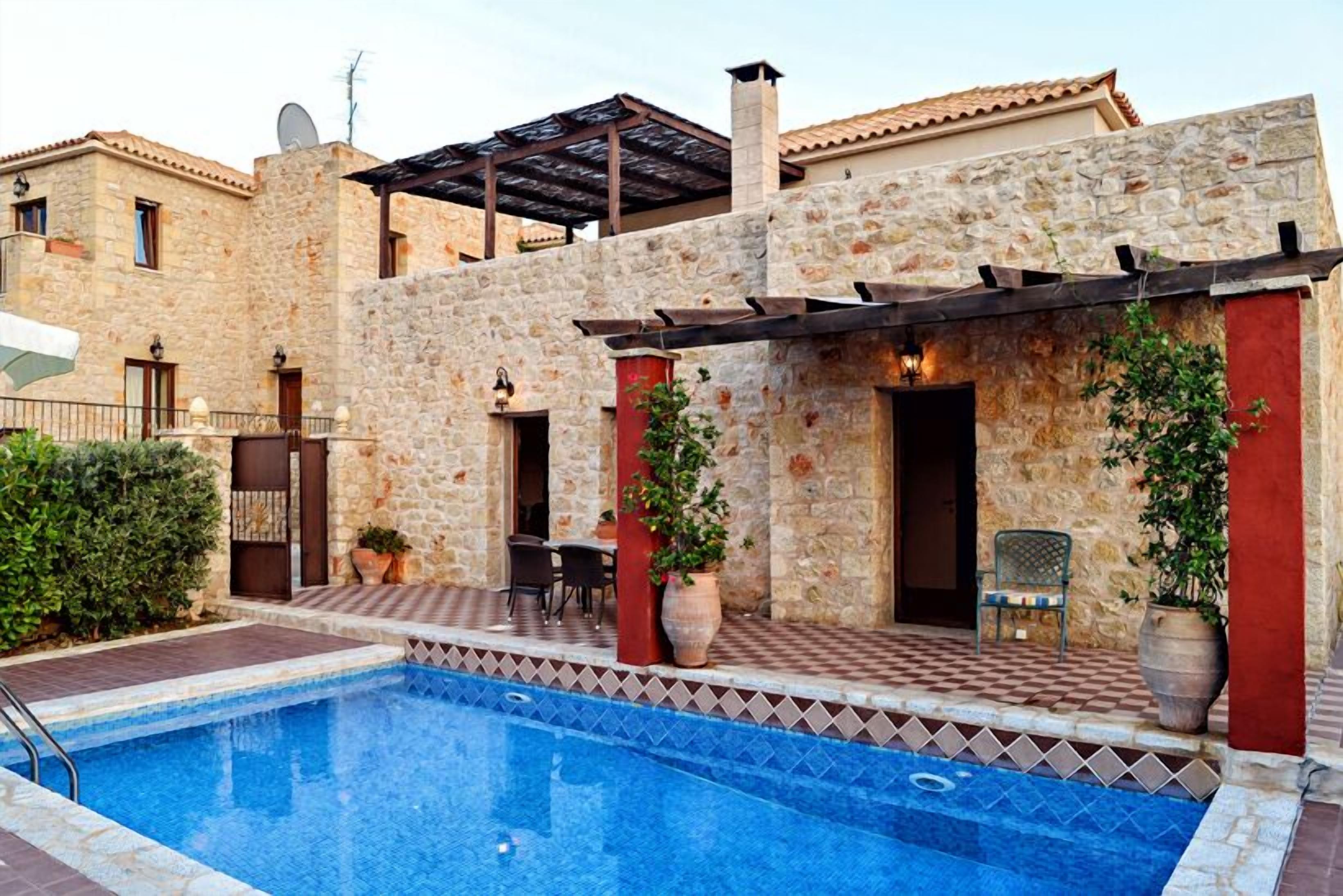 A stone building with a swimming pool, outdoor seating, and a pergola.