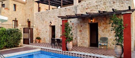 A stone building with a swimming pool, outdoor seating, and a pergola.