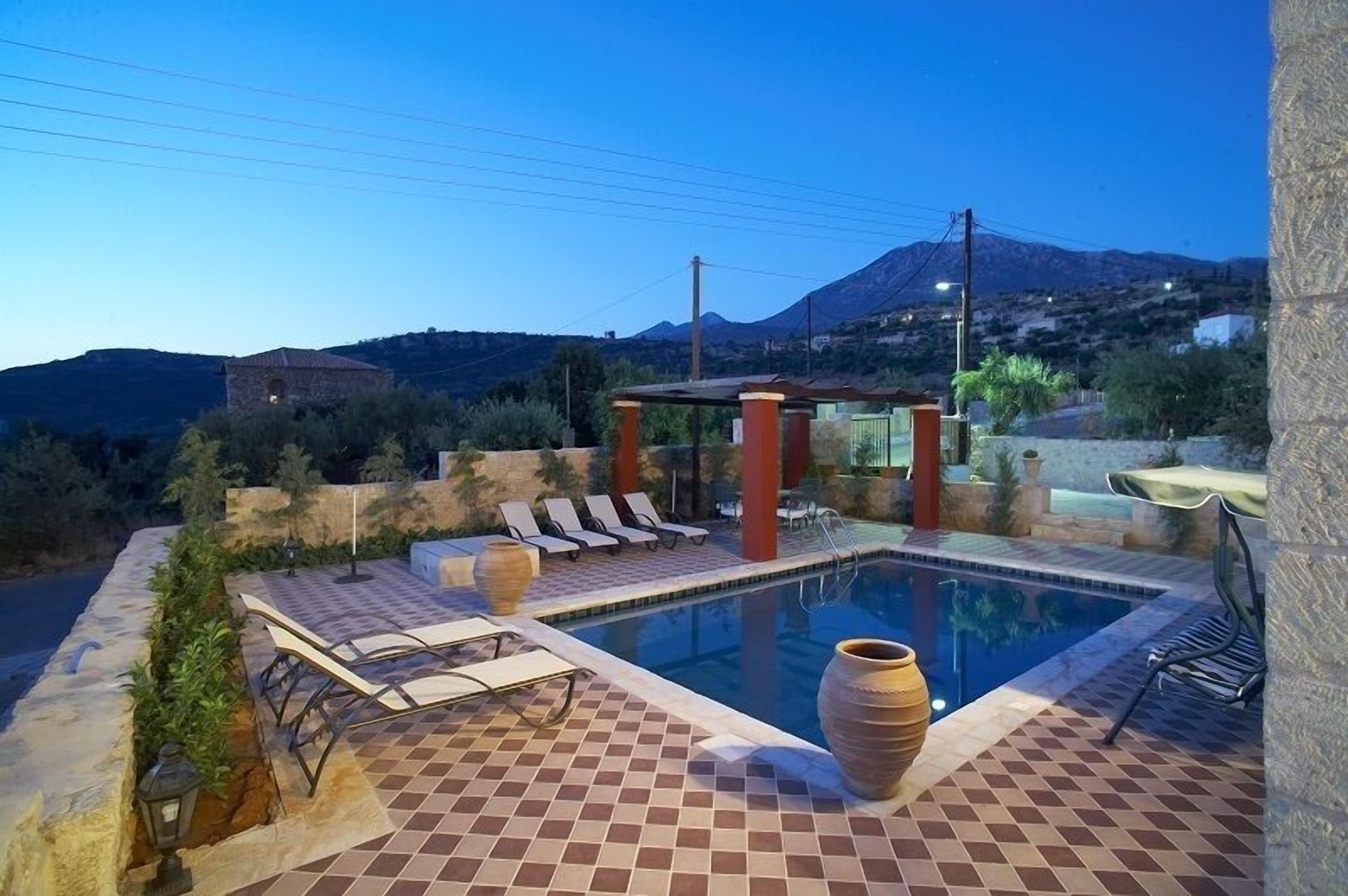 A swimming pool with lounge chairs, a pergola, and a mountain backdrop.