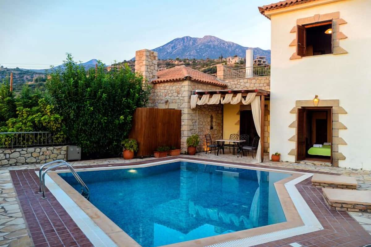 Una piscina con cubierta de piedra, un patio con mesa y sillas, y una montaña al fondo.