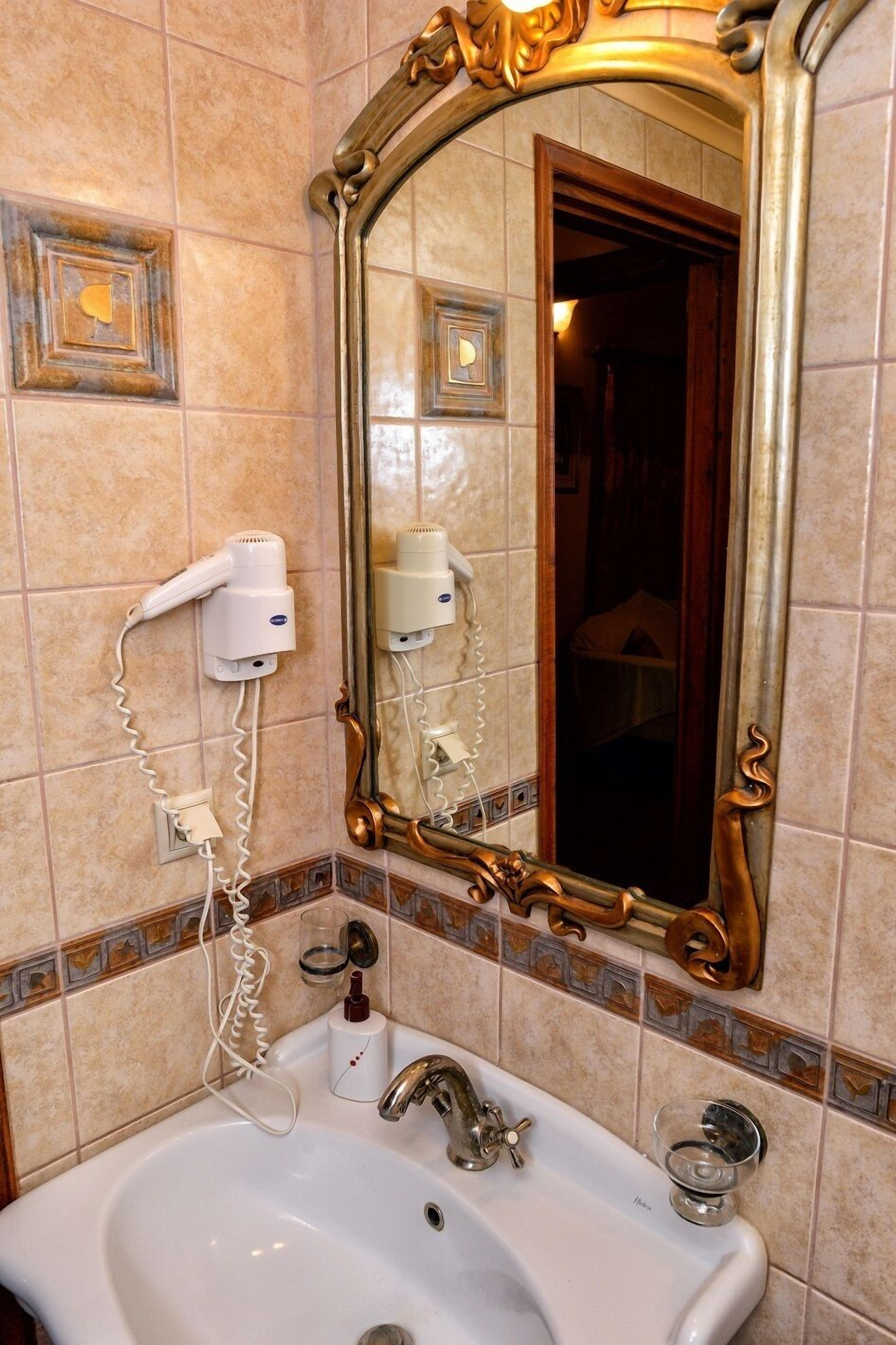 A bathroom with a large ornate mirror, a white sink, and a hairdryer mounted on the wall.